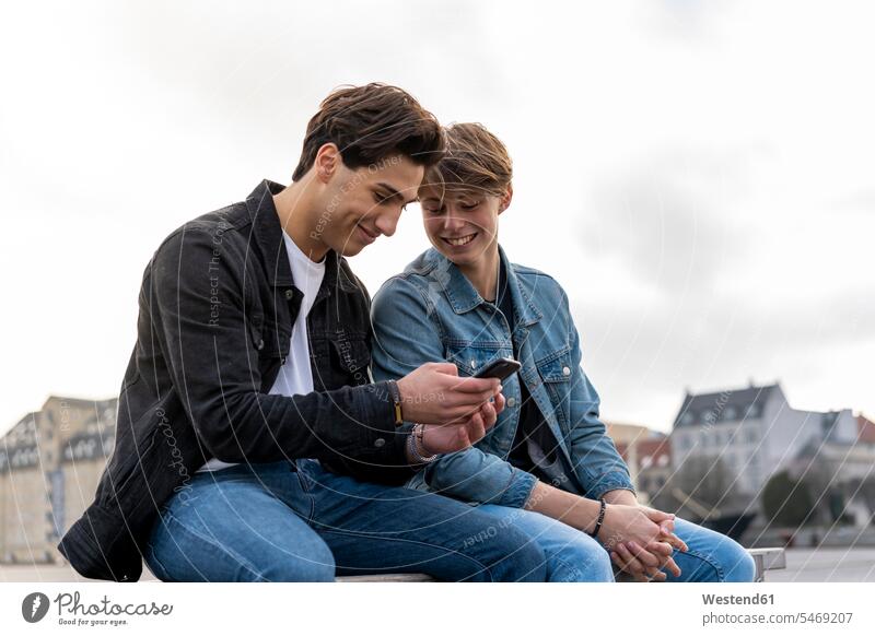 Denmark, Copenhagen, two young men sitting on a bench using cell phone Kobenhavn Traveller Travellers Travelers resting text messaging SMS Text Message