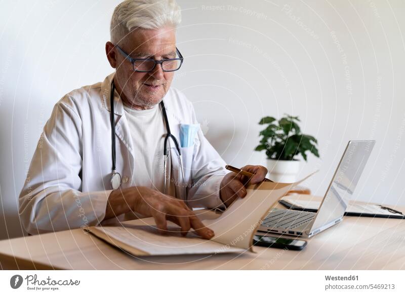Senior doctor looking at medical record while sitting in clinic color image colour image indoors indoor shot indoor shots interior interior view Interiors day