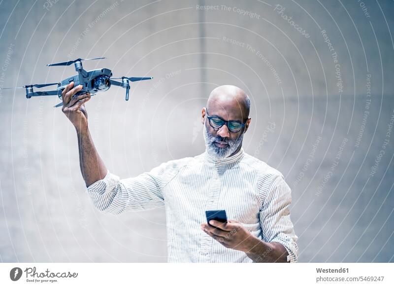 Portrait of bald mature man holding quadcopter while looking at cell phone Businessman Business man Businessmen Business men portrait portraits