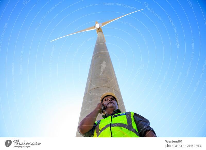 Low angle view of technician on cell phone in front of wind turbine wind turbines technicians on the phone call telephoning On The Telephone calling