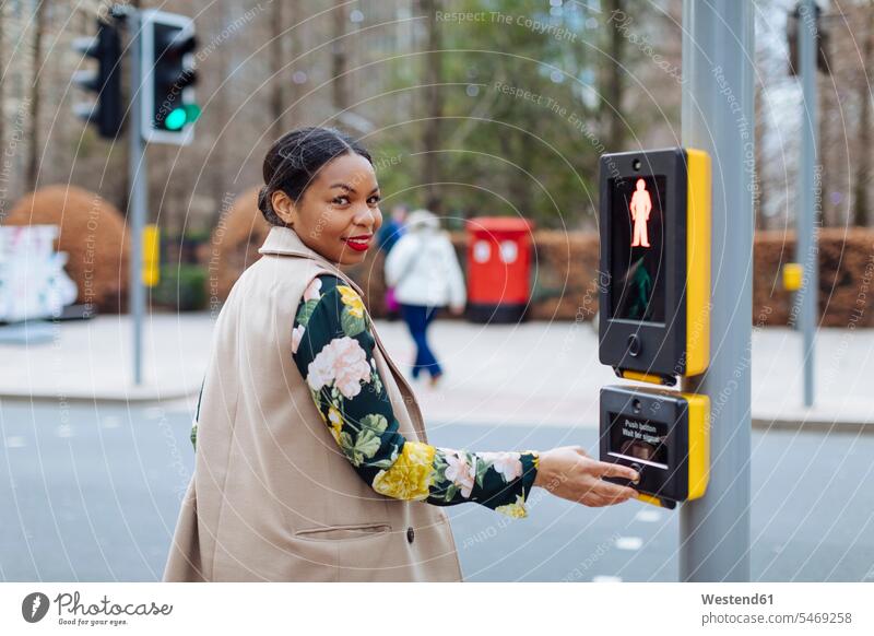 UK, London, portrait of smiling woman pressing button of pedestrian light smile pushing females women portraits pedestrian lights buttons Adults grown-ups
