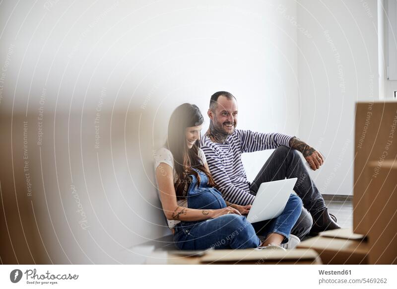 Happy couple working on laptop while sitting in domestic room color image colour image indoors indoor shot indoor shots interior interior view Interiors day