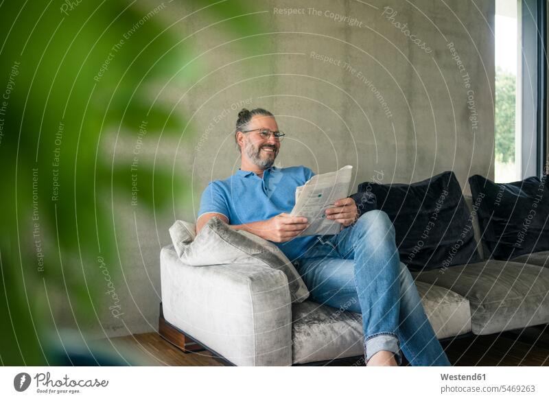 Smiling mature man sitting on couch at home reading newspaper human human being human beings humans person persons caucasian appearance caucasian ethnicity