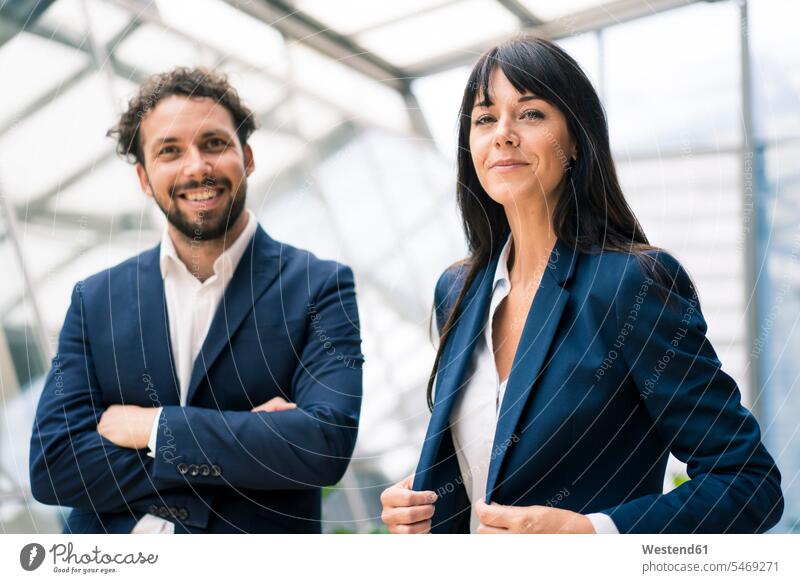 Smiling businesswoman with arms crossed standing by confident female colleague in office color image colour image indoors indoor shot indoor shots interior