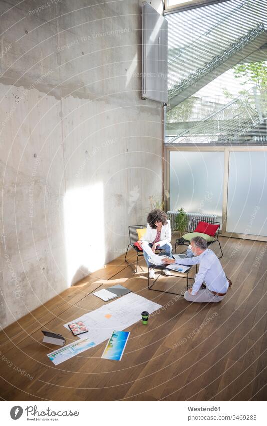 Businessman and businesswoman talking in a loft with documents on the floor Business man Businessmen Business men speaking lofts floors businesswomen
