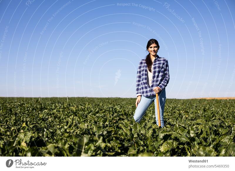 Young woman farmer with hoe on field Field Fields farmland females women farmhand smiling smile Adults grown-ups grownups adult people persons human being