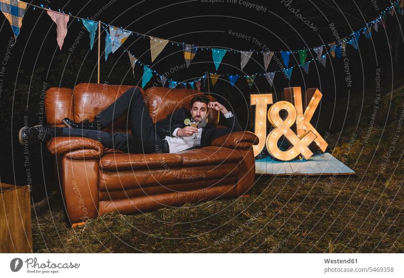 Portrait of man in suit posing on sofa on a night field party Party Parties Field Fields farmland men males portrait portraits Fullsuit suits full suit Wedding