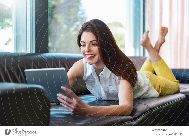 Smiling woman lying on couch at home using a tablet settee sofa sofas couches settees laying down lie lying down females women smiling smile digitizer