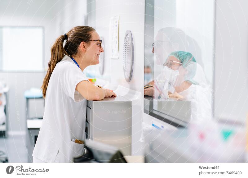 Smiling female doctor talking with coworker through window in pharmacy color image colour image Spain indoors indoor shot indoor shots interior interior view