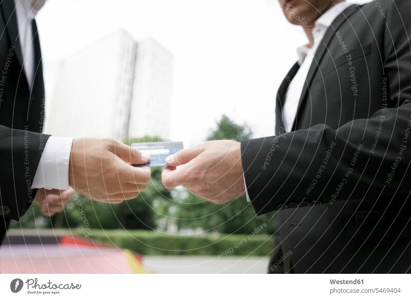 Two businessmen handing over credit card Businessman Business man Businessmen Business men debit card males giving give business people businesspeople
