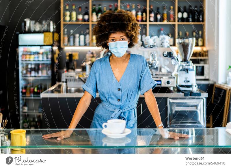 Young female owner wearing mask standing at cafe counter color image colour image indoors indoor shot indoor shots interior interior view Interiors day