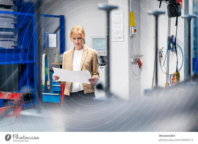Businesswoman looking at plan in factory businesswoman businesswomen business woman business women eyeing factories plans business people businesspeople