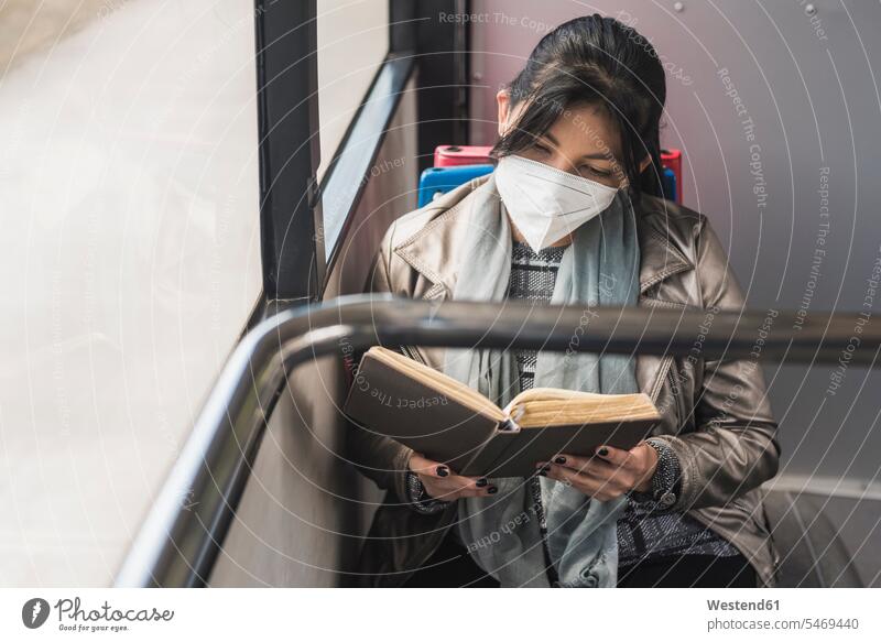Woman wearing protective mask while reading book in bus color image colour image Vehicle Interior Selective focus Differential Focus front view frontal head on