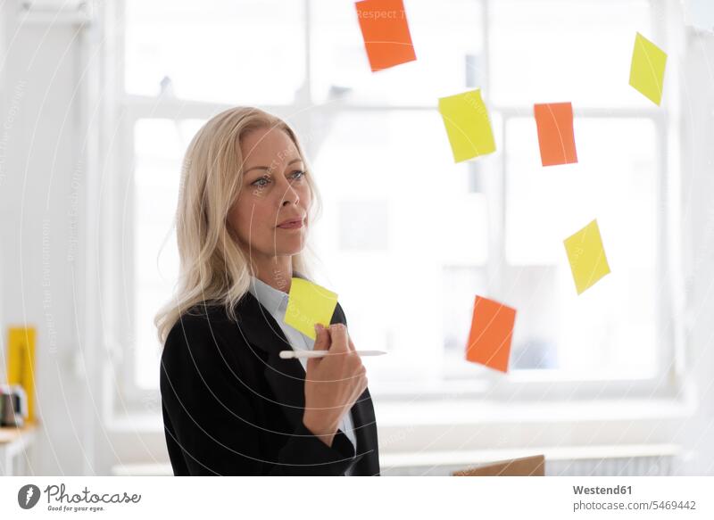 Businesswoman holding adhesive note contemplating in home office seen through window color image colour image Germany indoors indoor shot indoor shots interior