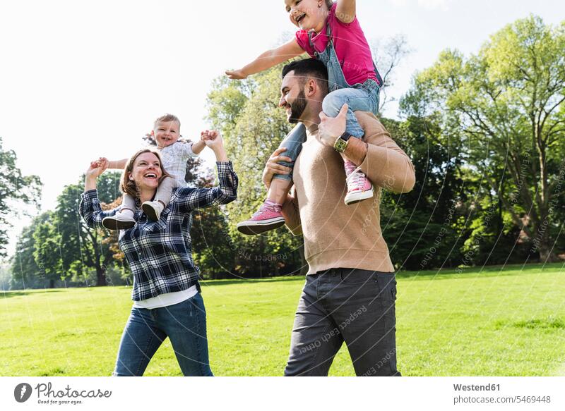 Happy parents carrying children on shoulders in a park family families piggyback piggy-back pickaback Piggybacking Piggy Back parks happiness happy people