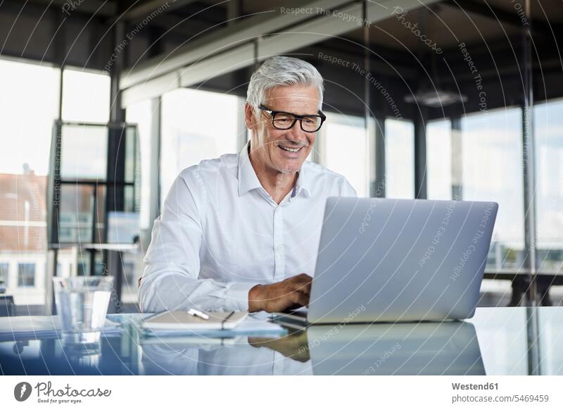 Businessman working in office, using laptop At Work Business man Businessmen Business men Office Offices desk desks using a laptop Using Laptops mature men
