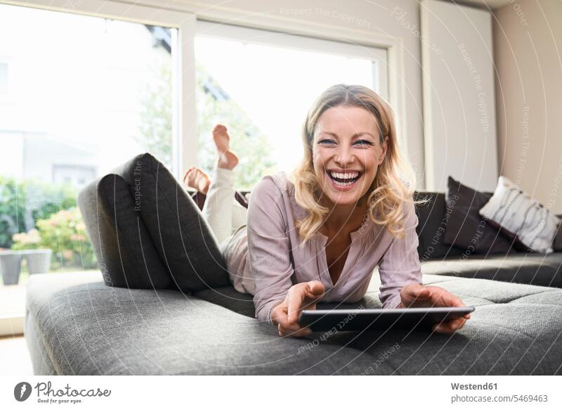 Portrait of laughing woman lying on couch at home using tablet laying down lie lying down portrait portraits digitizer Tablet Computer Tablet PC