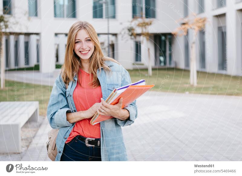 Smiling beautiful blond young woman holding books at university campus beautiful Woman beautiful Women people human being human beings humans person persons