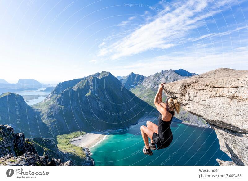 Mid adult woman hanging on edge of mountain at Ryten, Lofoten, Norway color image colour image outdoors location shots outdoor shot outdoor shots day