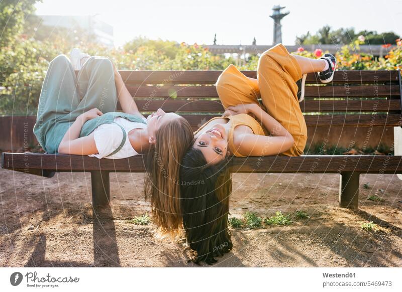 Two friends relaxing together on bench mate female friend benches Seated sit relaxation delight enjoyment Pleasant pleasure free time leisure time Lifestyle