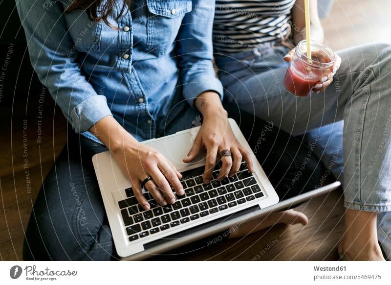 Close-up of two young women sitting on floor with soft drink and laptop woman females Seated refreshing drink soft drinks refreshing drinks female friends
