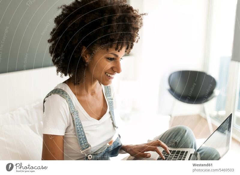Smiling woman sitting on bed using laptop females women beds Laptop Computers laptops notebook smiling smile Seated Adults grown-ups grownups adult people