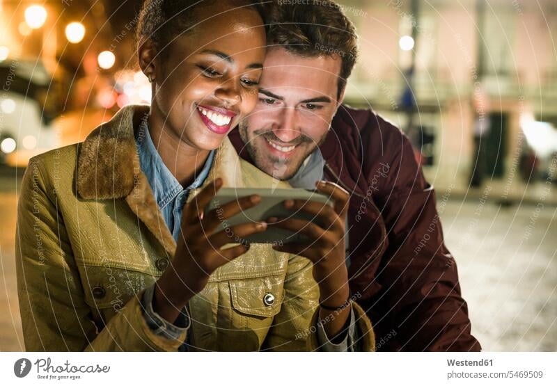 Portrait of happy young couple looking together at smartphone by night, Lisbon, Portugal telecommunication phones telephone telephones cell phone cell phones