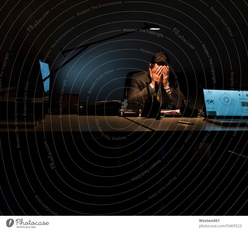 Overstressed businessman sitting at his desk in the dark office offices office room office rooms Seated desks night by night at night nite night photography