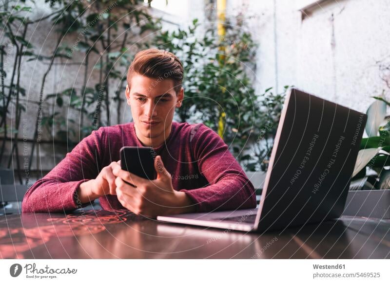 Young man sitting at table using cell phone and laptop Italy chatting self-employment self-employed Smartphone iPhone Smartphones freelancer freelancing Wifi