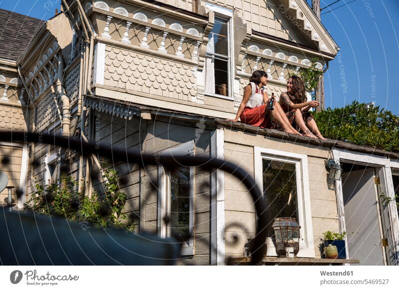 Two young women sitting on roof female friends Roof Seated woman females mate friendship Adults grown-ups grownups adult people persons human being humans