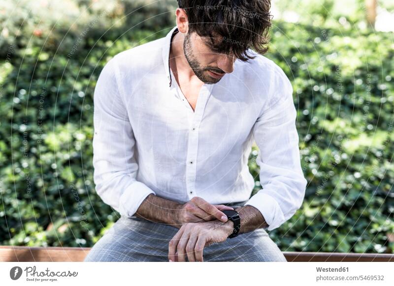 Young man sitting outdoors using smartwatch Seated smart watch men males Adults grown-ups grownups adult people persons human being humans human beings use