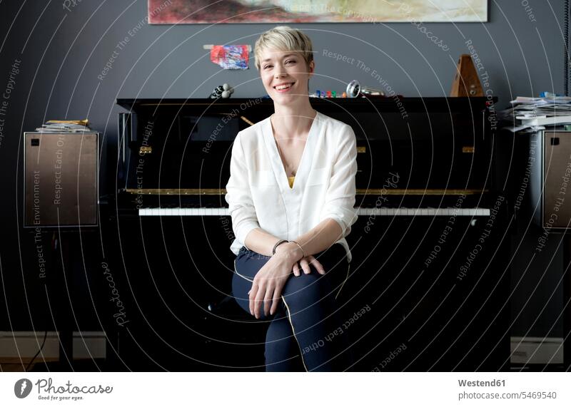 Portrait of laughing woman sitting in her music room in front of piano Germany Hugging Knees freelancer freelancing professional professionalism toothy smile