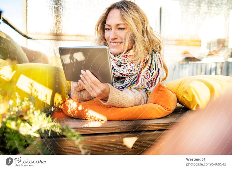 Portrait of smiling blond mature woman relaxing in winter garden using digital tablet winter gardens conservatory Sun Room Sunroom portrait portraits females