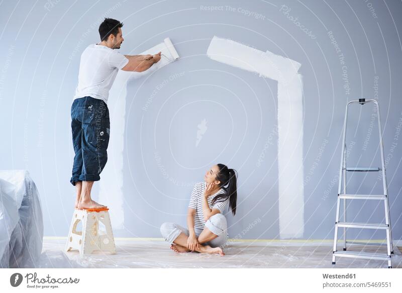 Couple painting house shape on wall in new apartment flat flats apartments houses couple twosomes partnership couples shapes walls people persons human being
