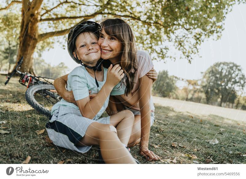 Mother embracing son sitting in public park on sunny day color image colour image outdoors location shots outdoor shot outdoor shots daylight shot