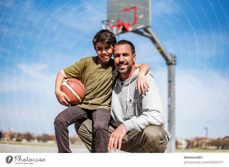 Portrait of happy father and son with basketball outdoors happiness smiling smile embracing embrace Embracement hug hugging portrait portraits sons manchild