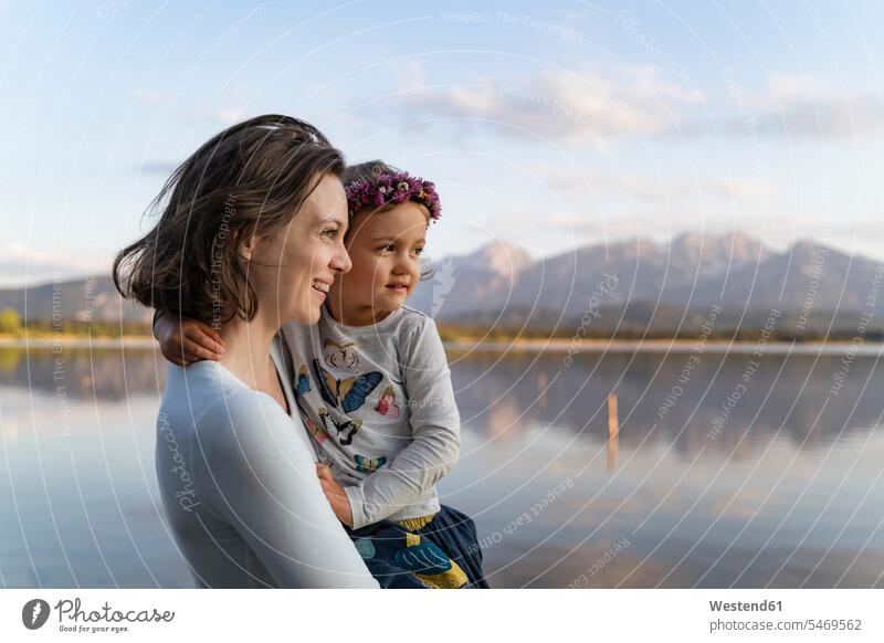 Smiling mother carrying cute daughter while standing against lake at sunset color image colour image Germany leisure activity leisure activities free time