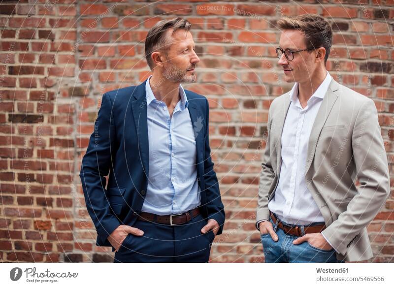 Two businessmen standing at brick building colleagues Businessman Business man Businessmen Business men brick wall brick walls business people businesspeople