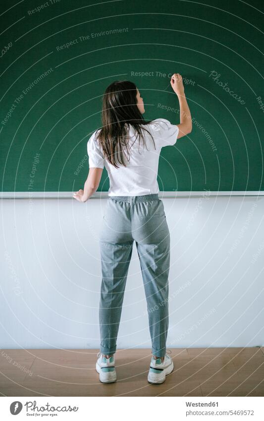 Full length rear view of young female student writing on blackboard in university classroom color image colour image University Student Students