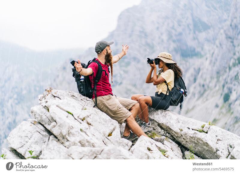 Young woman taking photo of man while sitting on mountain peak at Ruta Del Cares, Asturias, Spain color image colour image outdoors location shots outdoor shot