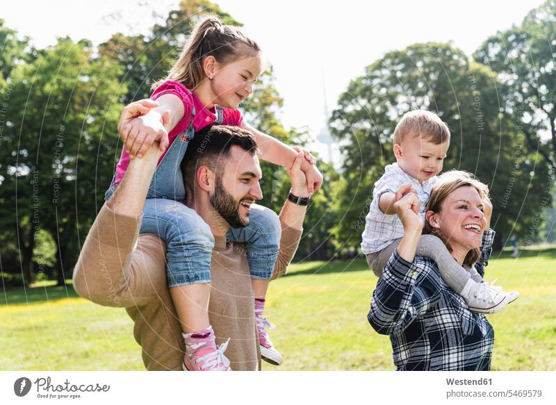 Happy parents carrying children on shoulders in a park family families happiness happy parks piggyback piggy-back pickaback Piggybacking Piggy Back people