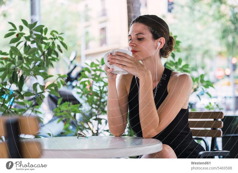 Young businesswoman sitting in coffee shop, taking a break, drinking tea Seated earphones ear phone ear phones Listening Music Tea Teas businesswomen