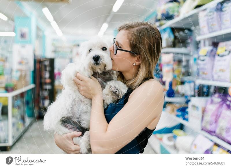 Close-up of female groomer kissing west highland white terrier in pet salon color image colour image Spain indoors indoor shot indoor shots interior