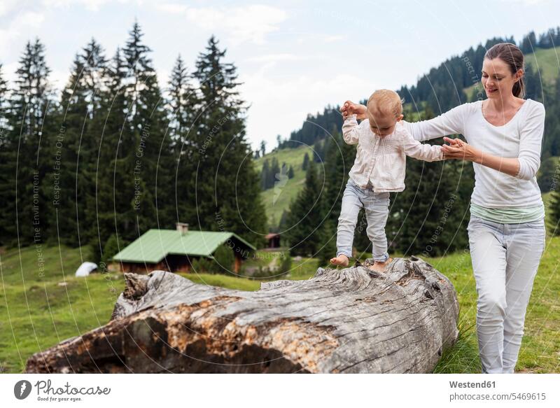 Germany, Bavaria, Oberstdorf, mother helping little daughter balancing on a log assistance assisting Help balance daughters mommy mothers mummy mama Support