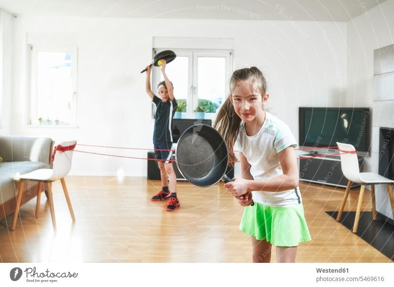 Smiling sister playing tennis with brother at home in quarantine color image colour image indoors indoor shot indoor shots interior interior view Interiors day