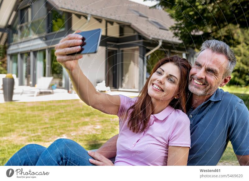 Happy couple sitting in garden of their home taking a selfie happiness happy house houses twosomes partnership couples gardens domestic garden Selfie Selfies