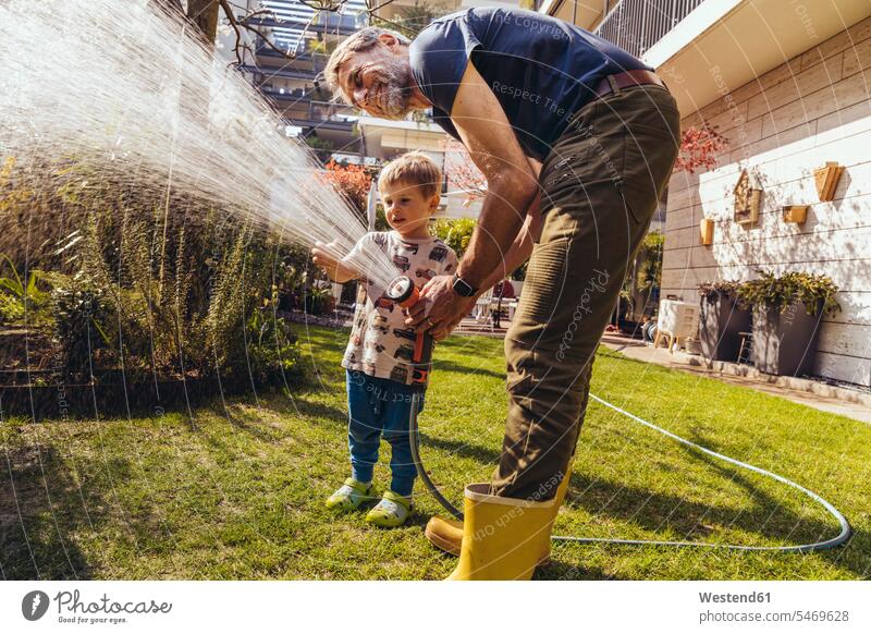 Father and son watering the lawn in garden T- Shirt t-shirts tee-shirt At Work work learn smile seasons summer time summertime summery delight enjoyment