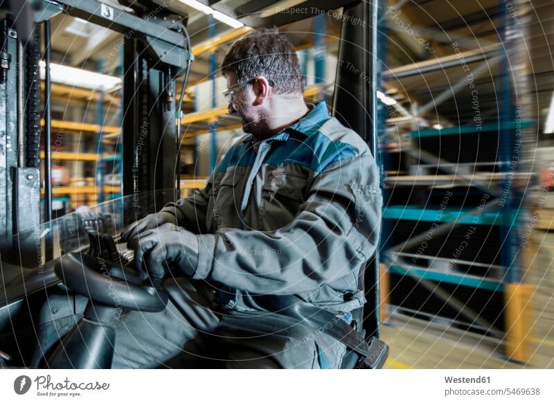 Fork-lift driver in motion in storehouse forklift forklifts forklift truck forklift trucks fork-lift driver worker blue collar worker workers blue-collar worker