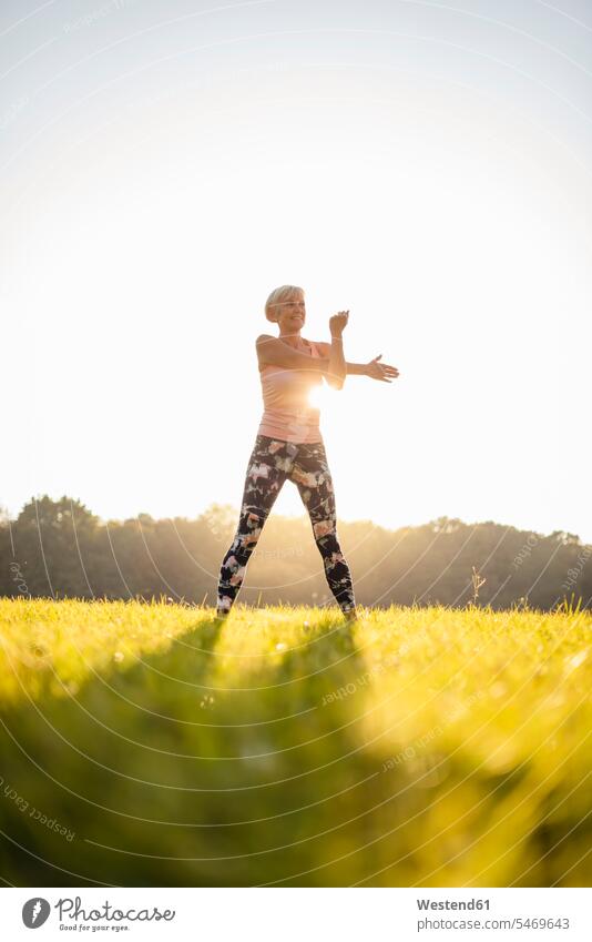 Senior woman stretching on rural meadow at sunset meadows country countryside sunsets sundown females women senior women elder women elder woman old