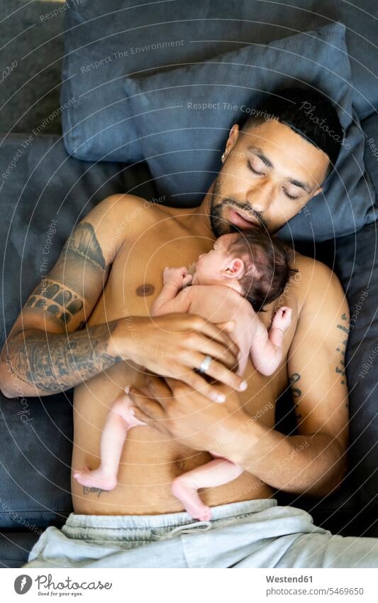 Father lying on couch with nude newborn baby Spain skin contact skin to skin tattooed one parent comfortable resting fatherhood paternity body bodies